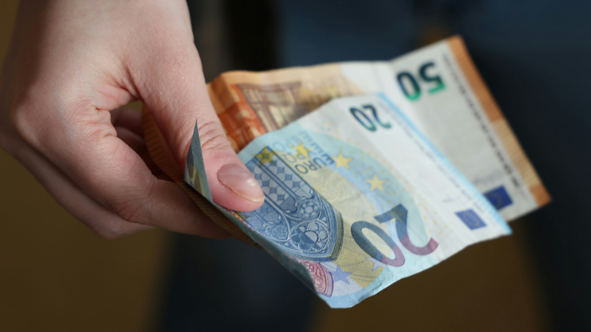 Eine Hand hält einen 20- und einen 50-Euro-Schein