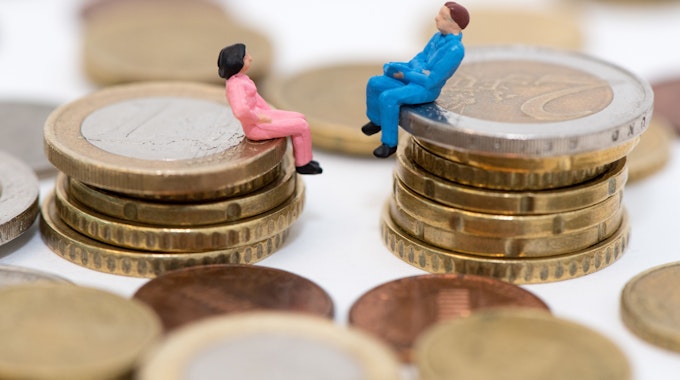 Zwei kleine Figuren, ein Mann und eine Frau, sitzen auf einem Stapel Geldmünzen