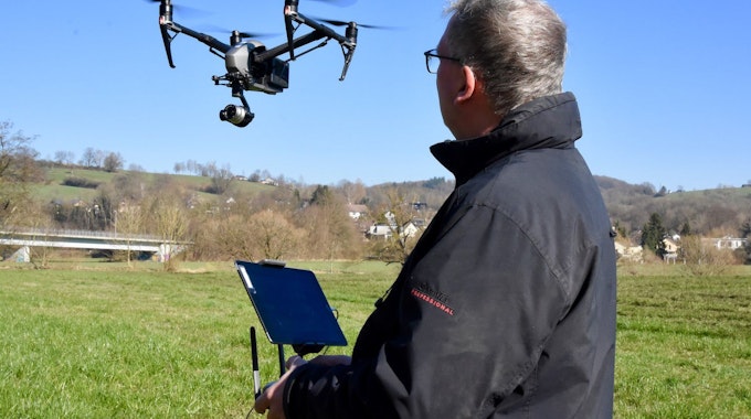 Andreas Müller-Goldkuhle steht auf einem grünen Feld, vor ihm in der Luft fliegt eine Drohne.