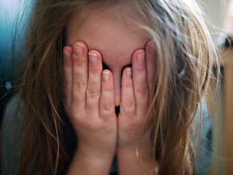 Ein junges Mädchen hält sich die Hände vor ihr Gesicht.