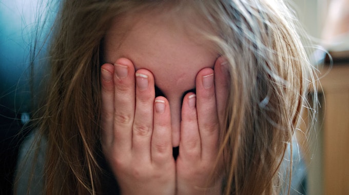 Ein junges Mädchen hält sich die Hände vor ihr Gesicht.