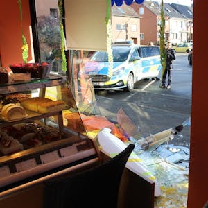 Das Foto zeigt eine zerstörte Glasscheibe und einen Polizeiwagen vor der Bäckerei.