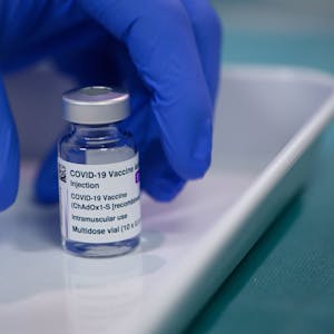 Eine Ampulle des Impfstoffs Vaxzevria von&nbsp;Astrazeneca, die von einer Hand mit einem blauen Handschuh genommen wird.