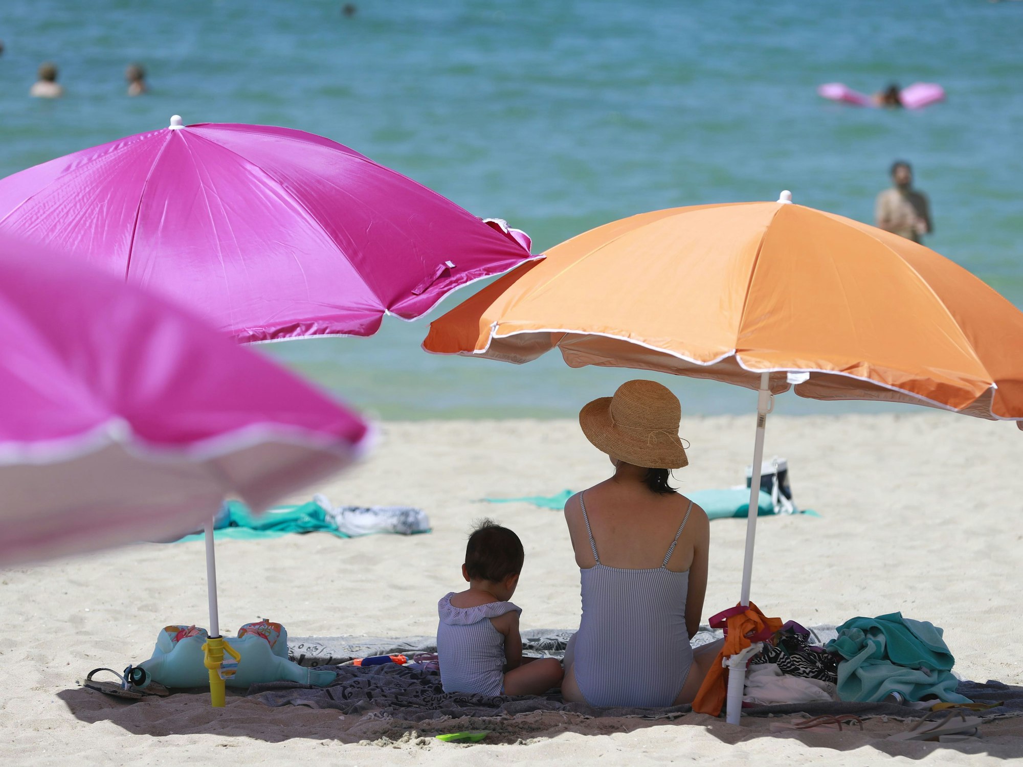Eine Frau sitzt neben ihrem Kind unter einem Sonnenschirm an einem warmen Sommertag am Strand, hier im August 2022 auf Mallorca.