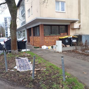 Das Bild zeigt das Haus August-Haas-Straße 1, mit der leerstehenden Gaststätte im Erdgeschoss. In der Umgebung sammelt sich der Müll.