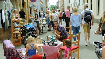 Ein mann sitzt mit zwei Kindern an einem Tisch mitten auf dem Bürgersteig