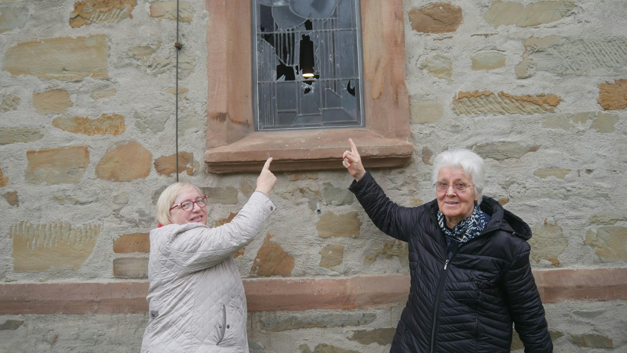 Zwei Frauen zeigen auf ein kaputtes Kirchenfenster.