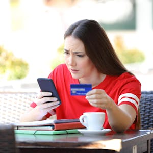 Eine Frau blickt auf ein Handy und hält eine Kreditkarte.