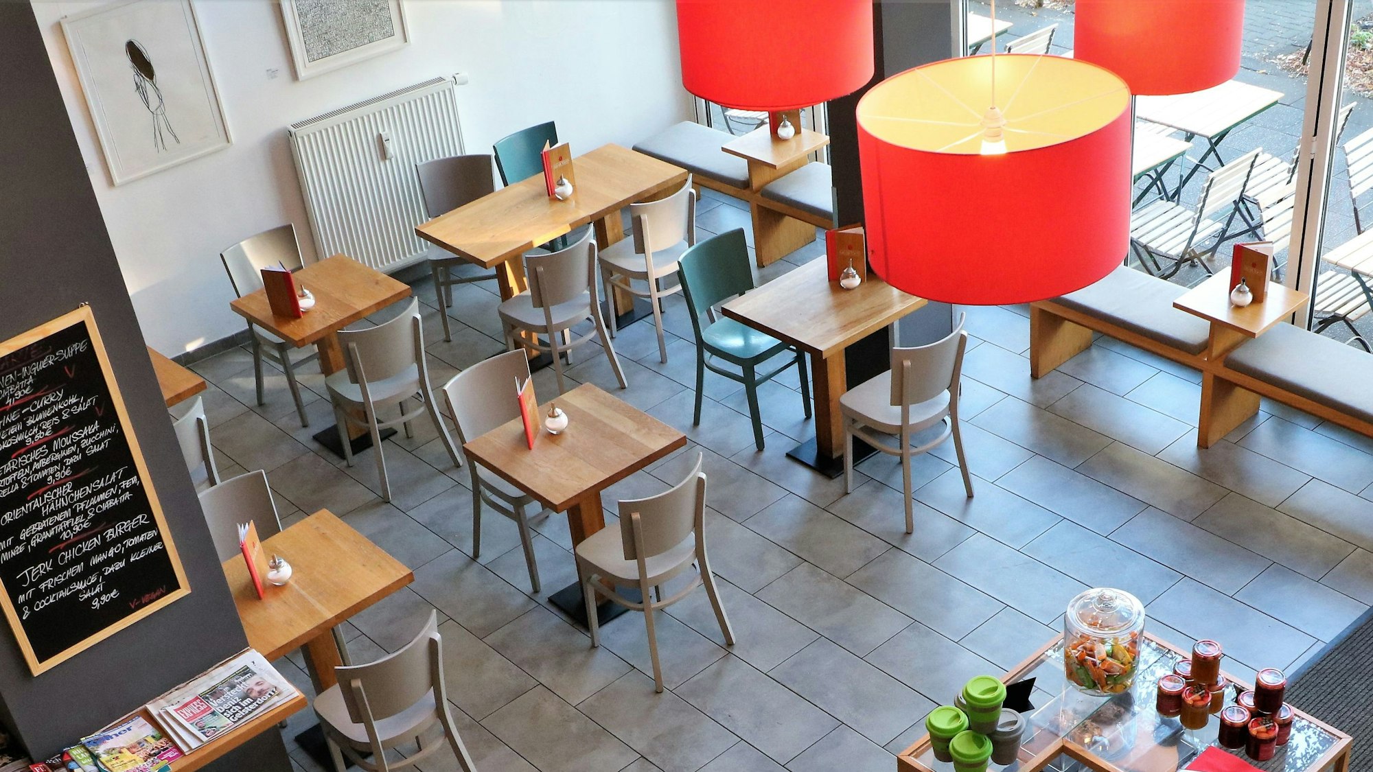 Das Café „Wo ist Tom?“: Aufgenommen aus dem zweiten Stock des Cafés, sind Tische und die Kuchentheke zu sehen. Es hängt eine auffällige rote Lampe herunter.