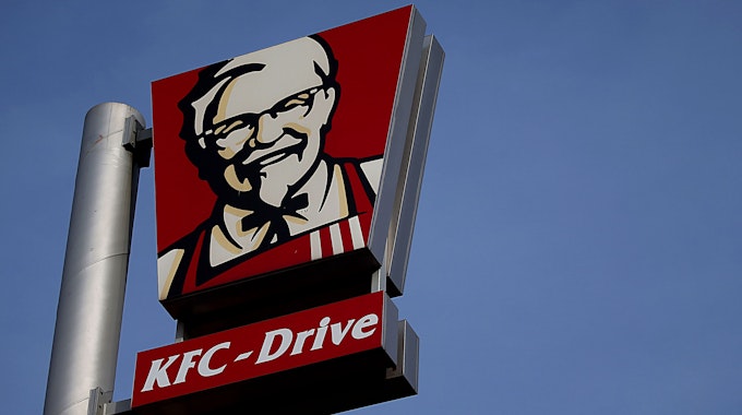 Das Symbolfoto aus dem Jahr 2018 zeigt einen Metall-Mast, an dem zwei große Schilder des US-Fast-Food-Konzerns Kentucky Fried Chicken befestigt sind. Im Hintergrund ist blauer Himmel zu sehen.