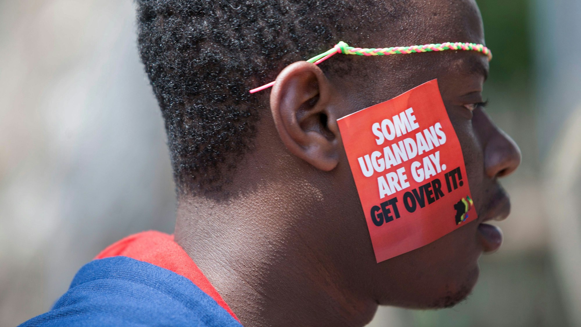 dpatopbilder - ARCHIV - 08.08.2014, Uganda, Entebbe: Ein ugandischer Mann trägt einen Aufkleber mit der Aufschrift "Some Ugandans Are Gay. Get Over It" ("Einige Ugander sind schwul. Finde dich damit ab") während der  LGBT-Pride-Feierlichkeiten auf seiner Wange. Die ugandische Regierung hat ein Gesetz verabschiedet, das Gefängnisstrafen von bis zu zehn Jahren für Straftaten im Zusammenhang mit gleichgeschlechtlichen Beziehungen vorsieht und damit auf die Stimmung in der Bevölkerung reagiert, aber auch den Druck auf die LGBTQ-Gemeinschaft des ostafrikanischen Landes erhöht. Foto: Rebecca Vassie/AP/dpa +++ dpa-Bildfunk +++
