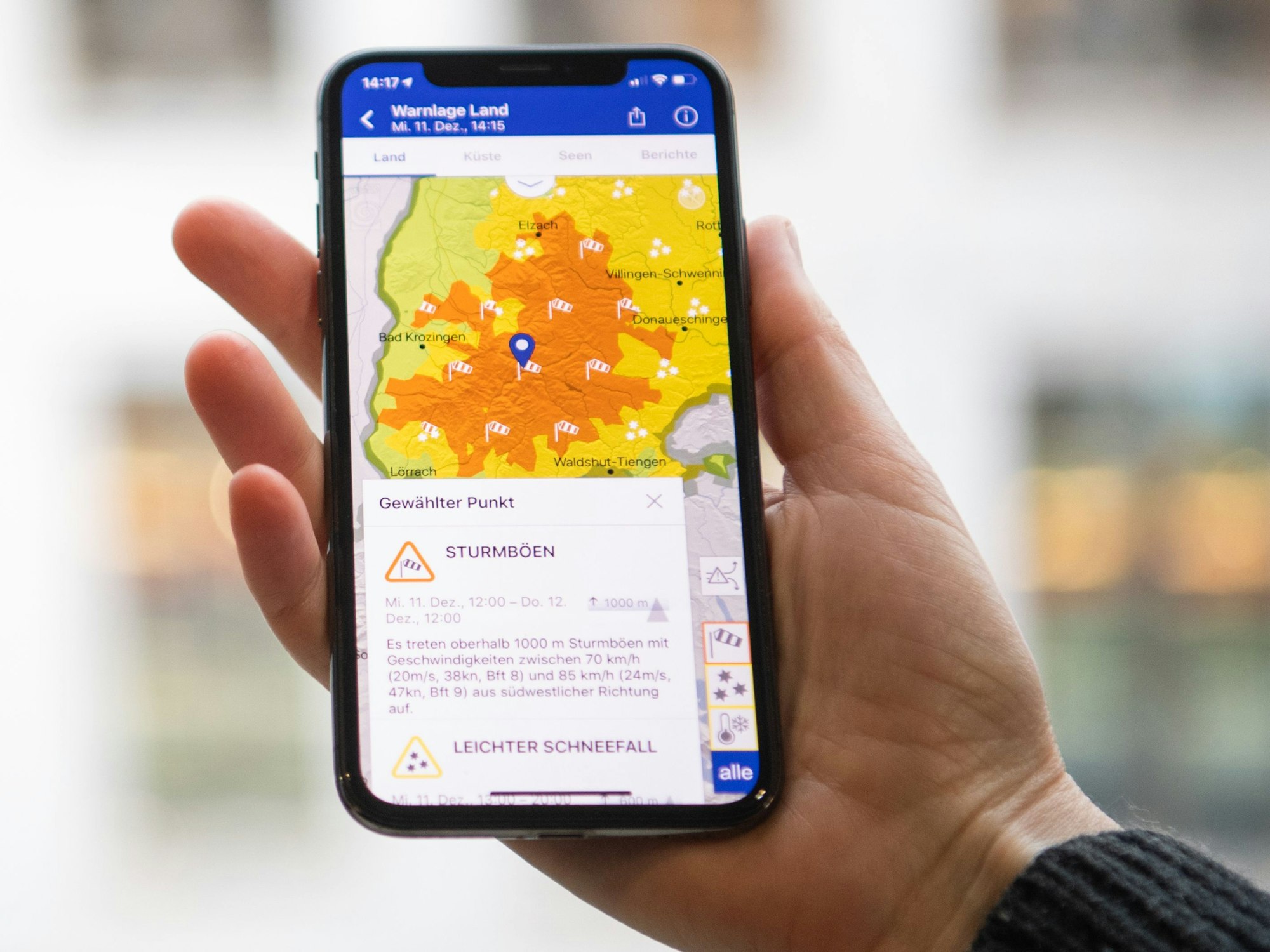 Das Symbolfoto aus dem Jahr 2019 zeigt eine Hand, die ein Smartphone hält. Auf dem Bildschirm sieht man eine Wetterkarte in gelb-orange, darunter steht Text.