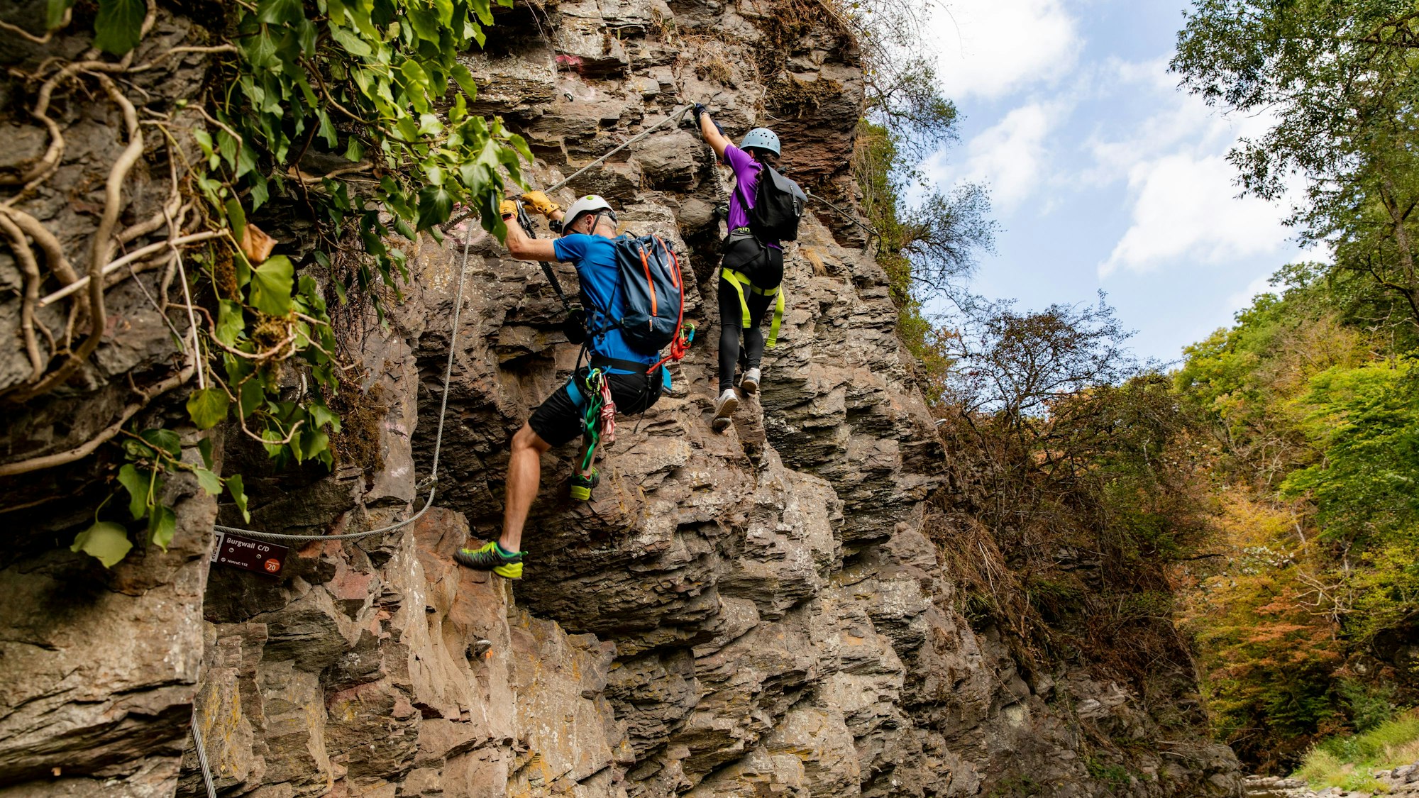 ein Mann und eine Frau klettern mit Sicherheitsausrüstung an einem Felsen