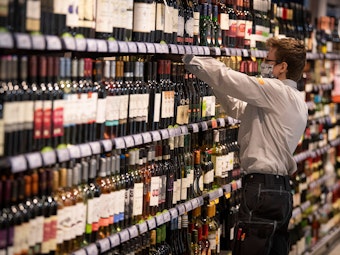 Ein Mitarbeiter in einem Supermarkt, hier im Juli 2020, sortiert in einer Filiale in Frankfurt am Main Alkohol in einem Regal.