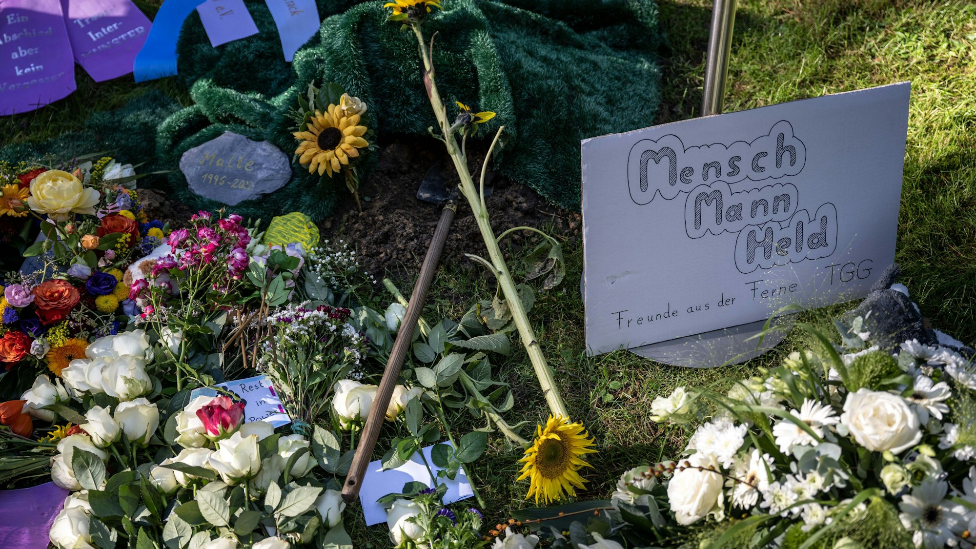 Ein Plakat mit der Aufschrift „Mensch, Mann, Held“ liegt neben Blumen am Grab des verstorbenen Malte C. bei Münster.