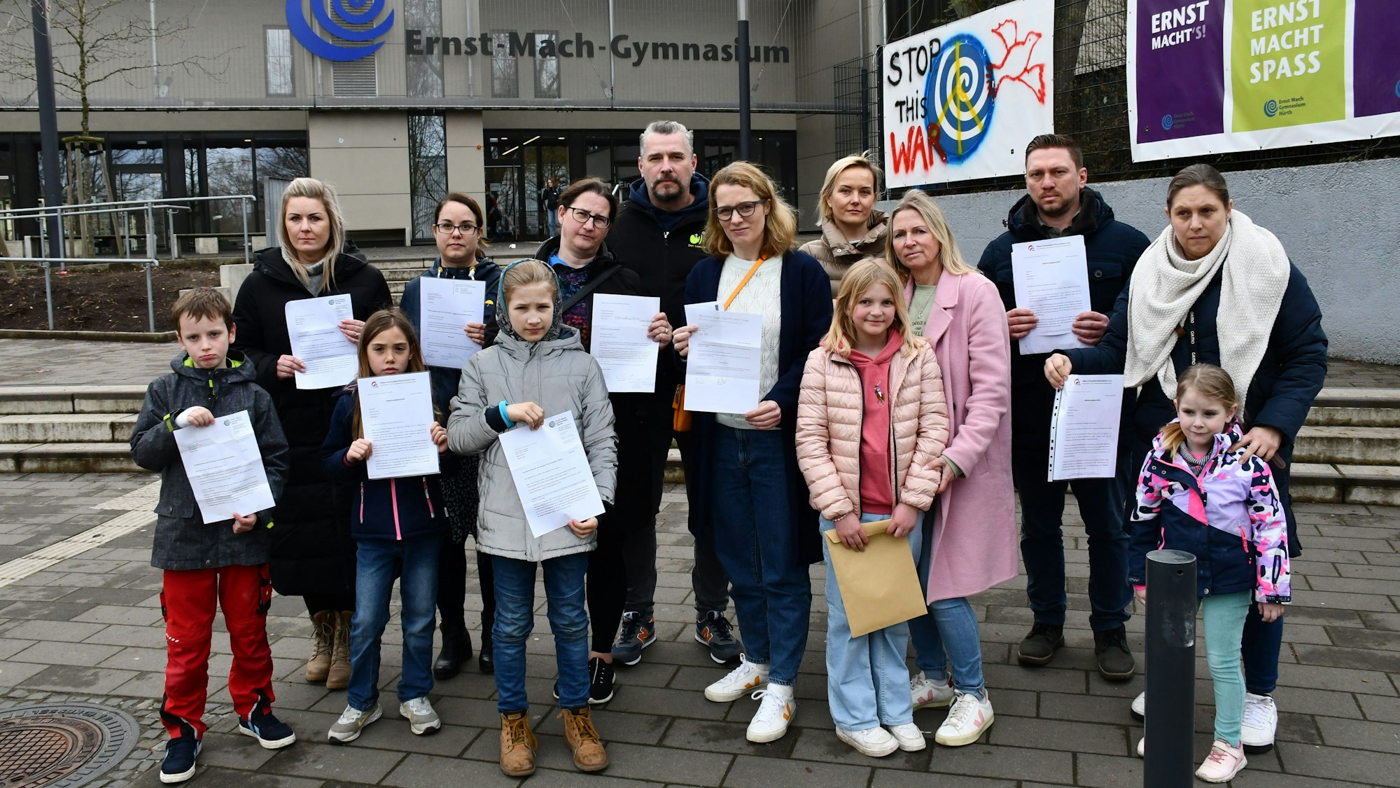 Eltern und Kinder stehen mit Zetteln in der Hand vor dem Ernst-Mach-Gymnasium.