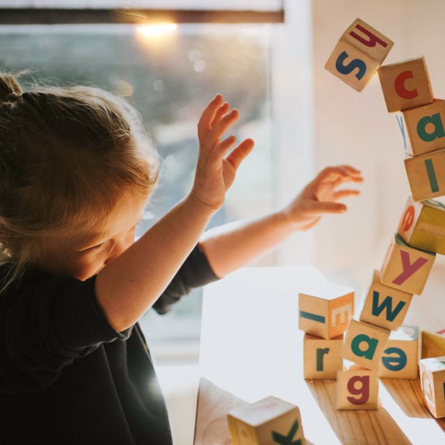 Ein kleines Mädchen baut einen Turm mit Lernbauklötzen auf denen Buchstaben stehen