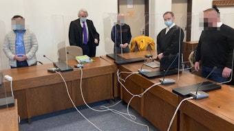 Das Foto zeigt die drei Angeklagten und ihre Verteidiger beim Prozessauftakt im Februar 2022 vor dem Landgericht in Köln.