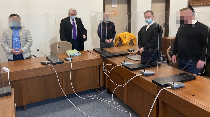 Das Foto zeigt die drei Angeklagten und ihre Verteidiger beim Prozessauftakt im Februar 2022 vor dem Landgericht in Köln.