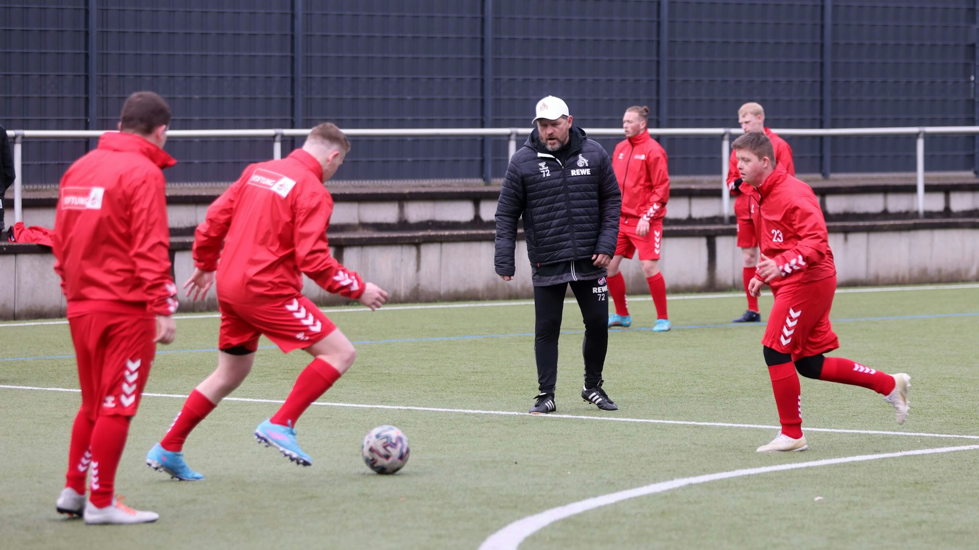 FC-Trainer Steffen Baumgart steht zwischen mehreren Männern, die sich einen Ball zuschießen.