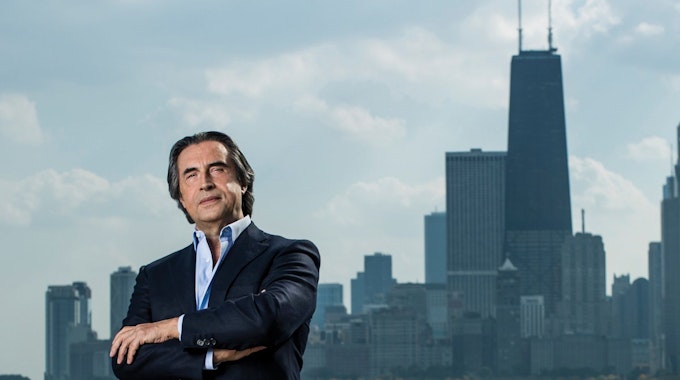 Riccardo Muti steht am Ufer des Chicago River, im Hintergrund die Stadtsilhouette.