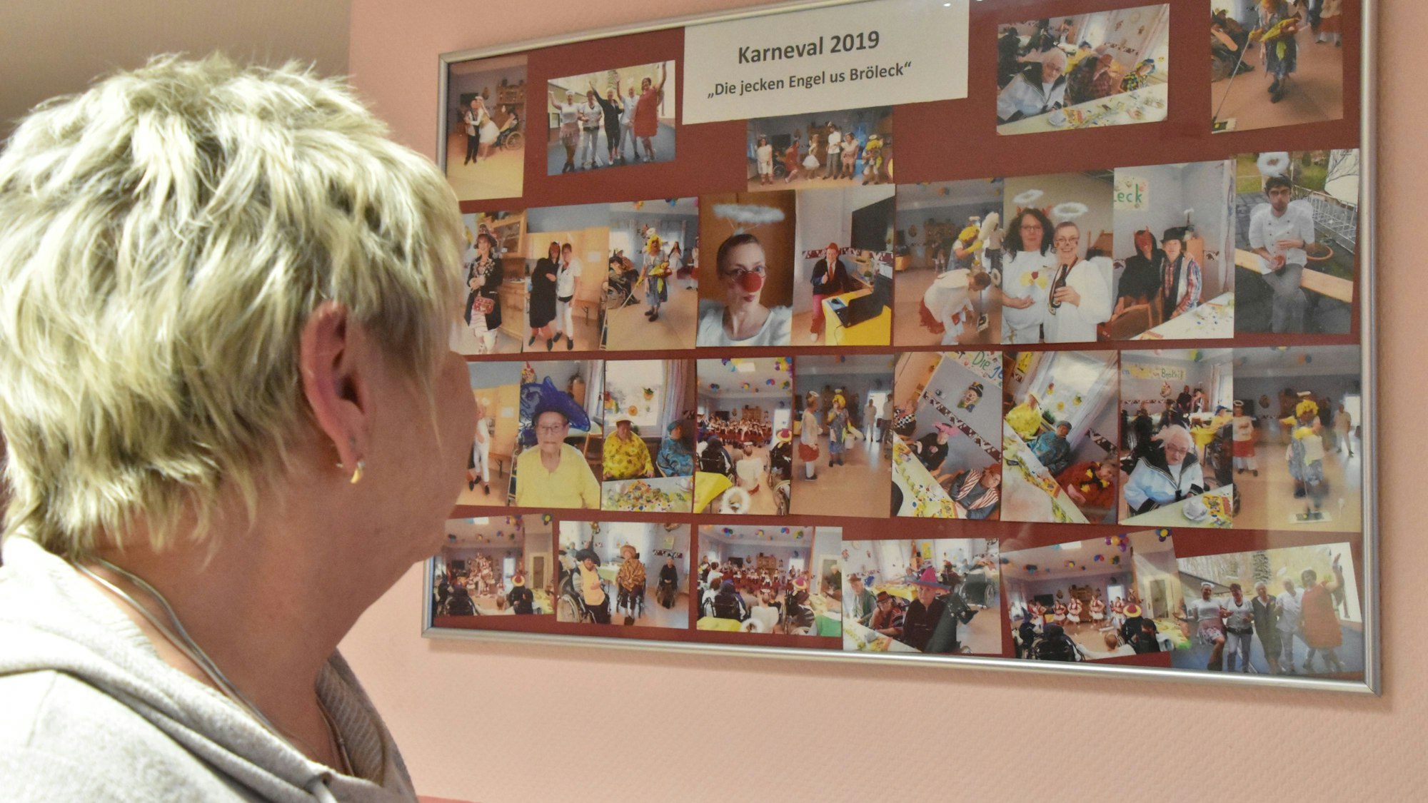 Eine Frau schaut auf eine Fotocollage an der Wand, mit Bildern von Personal und Bewohnern bei Feierlichkeiten.