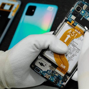 Das Bild zeigt eine Person in weißen Handschuhen, die ein defektes Smartphone repariert.
