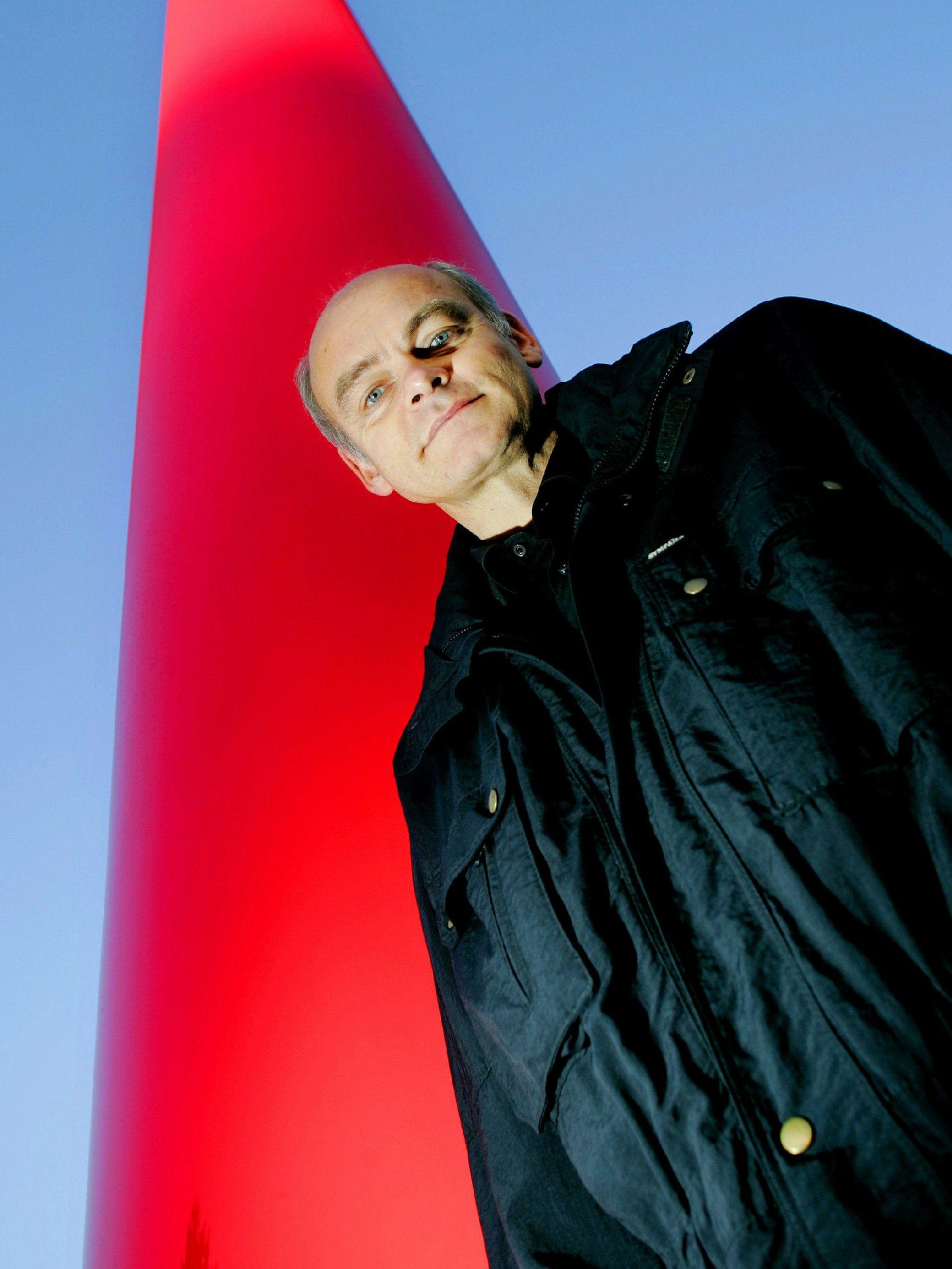 Der Kölner Künstler Lutz Fritsch steht neben einer leuchtend roten Riesen-Stele im Kölner Verteilerkreis.