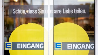 Das Symbolfoto aus dem Jahr 2020 zeigt die Eingangstüren einer Edeka-Filiale. Auf das Glas sind ein gelbes Herz, das Edeka-Logo sowie die Schriftzüge „Eingang“ und „Schön, dass Sie unsere Liebe teilen.“ gedruckt.
