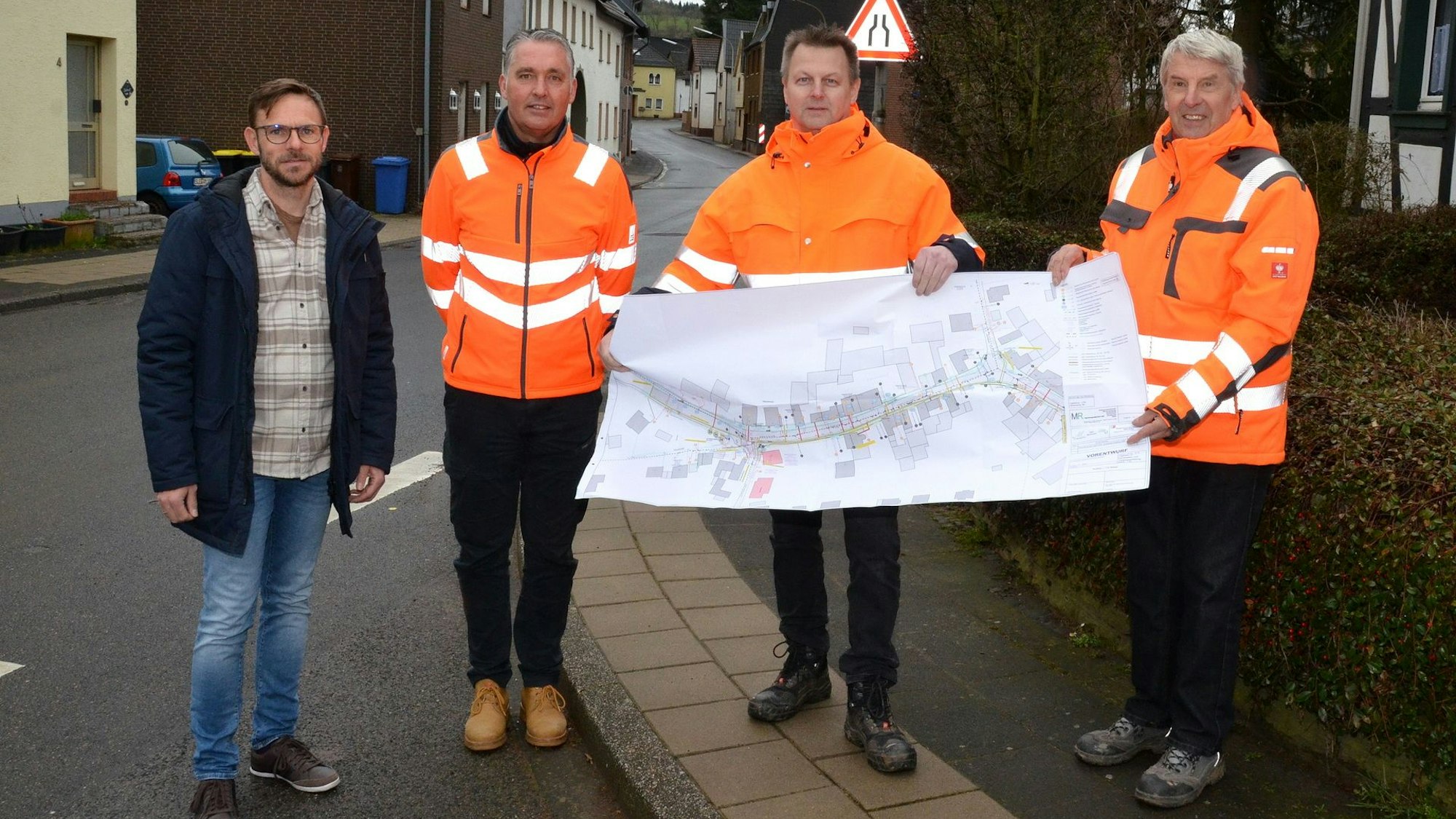 Drei Männer mit orangen Warnwesten halten einen Stadtplan hoch. Daneben steht ein Mann in Straßenklamotten.