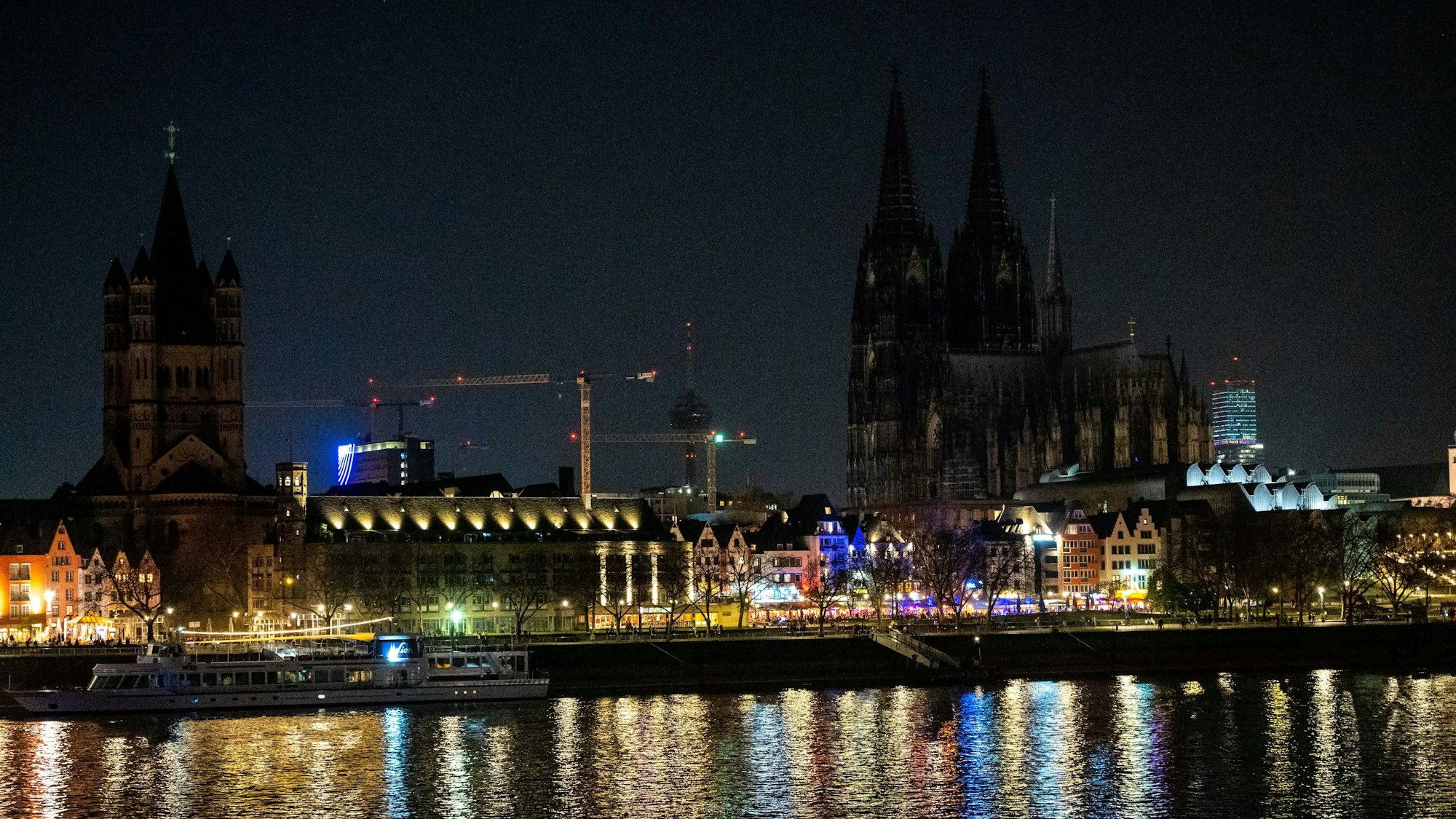 Das Bild zeigt die dunkle Skyline Kölns mit wenigen beleuchteten Altstadthäusern.