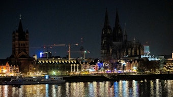 Das Bild zeigt die dunkle Skyline Kölns mit wenigen beleuchteten Altstadthäusern.
