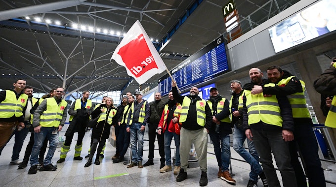 Streikende Mitarbeiterinnen und Mitarbeiter des Flughafens Stuttgart stehen am 17. März 2023 mit Westen der Gewerkschaft Verdi in der leeren Abflughalle im Stuttgarter Flughafen.