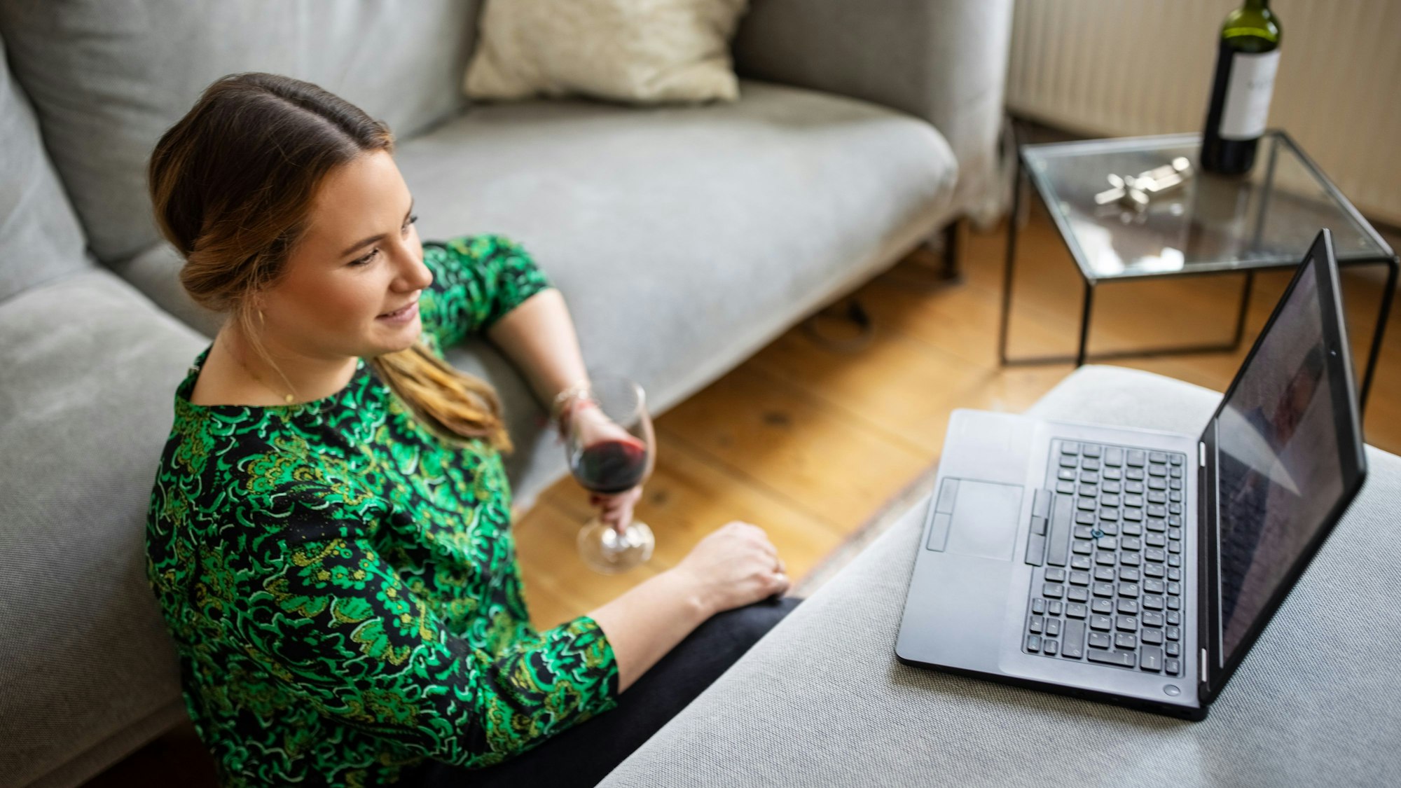 Eine Frau sitzt mit einem Glas Rotwein vor ihrem Laptop.