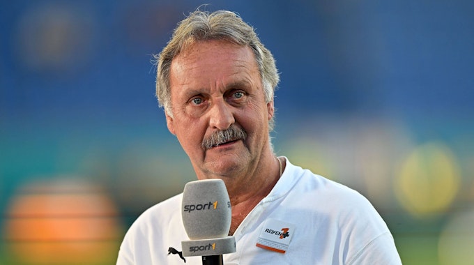 Peter Neururer hält als Sport1-Experte ein Mikrofon des Senders in der Hand.