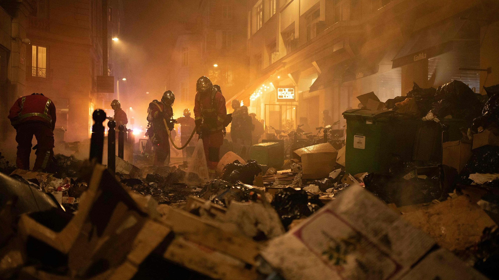 Paris: Feuerwehrleute kontrollieren Müll nach dem Löschen eines Feuers während einer Demonstration. In Frankreich haben sich die Streiks und Proteste gegen die Rentenreform zugespitzt.