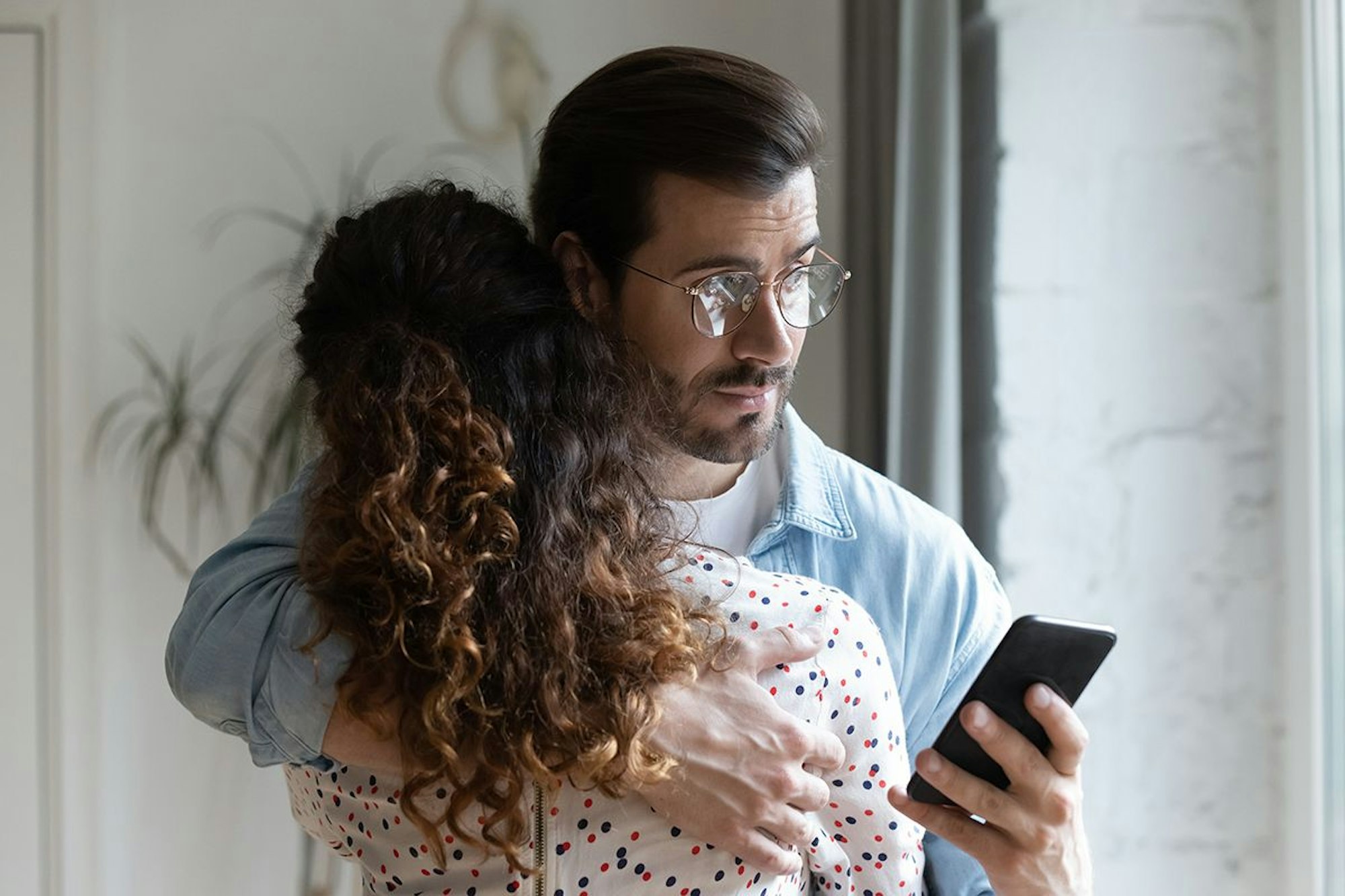 Mann hält Frau im Arm und schaut auf sein Handy
