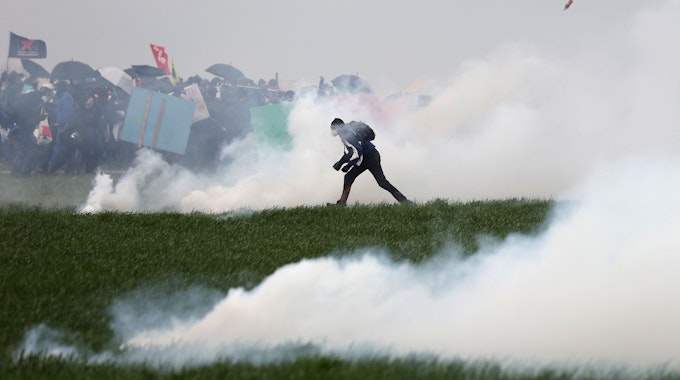 Ein Demonstrant steht inmitten von Tränengas auf einem Feld. Im Hintergrund sind weitere Demonstranten zu erkennen.