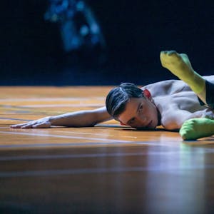 Szene aus „Ballet of (Dis)Obedience“ von Choreograf Richard Siegal. Ein Tänzer streckt sich am Boden. Einen Arm hat er ausgestreckt, den Unterkörper abgewinkelt. Mit der anderen Hand hält er einen Fußknöchel.