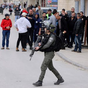 Ein Istraelischer Soldat läuft vor mehreren Demonstrierenden auf einer Straße.&nbsp;