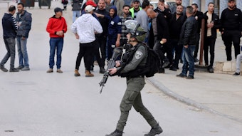 Ein Istraelischer Soldat läuft vor mehreren Demonstrierenden auf einer Straße.