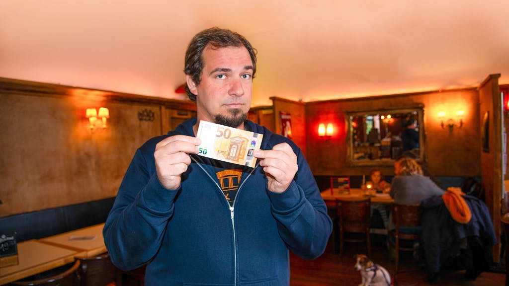 Christoph Specht, Kellner in der „Geissel“ auf der Aachener Straße, hält einen 50-Euro-Schein in die Kamera. Er ärgert sich mit seinen Kollegen oft über geplatzte Reservierungen. Eine Strafgebühr hält er für eine gute erzieherische Maßnahme.