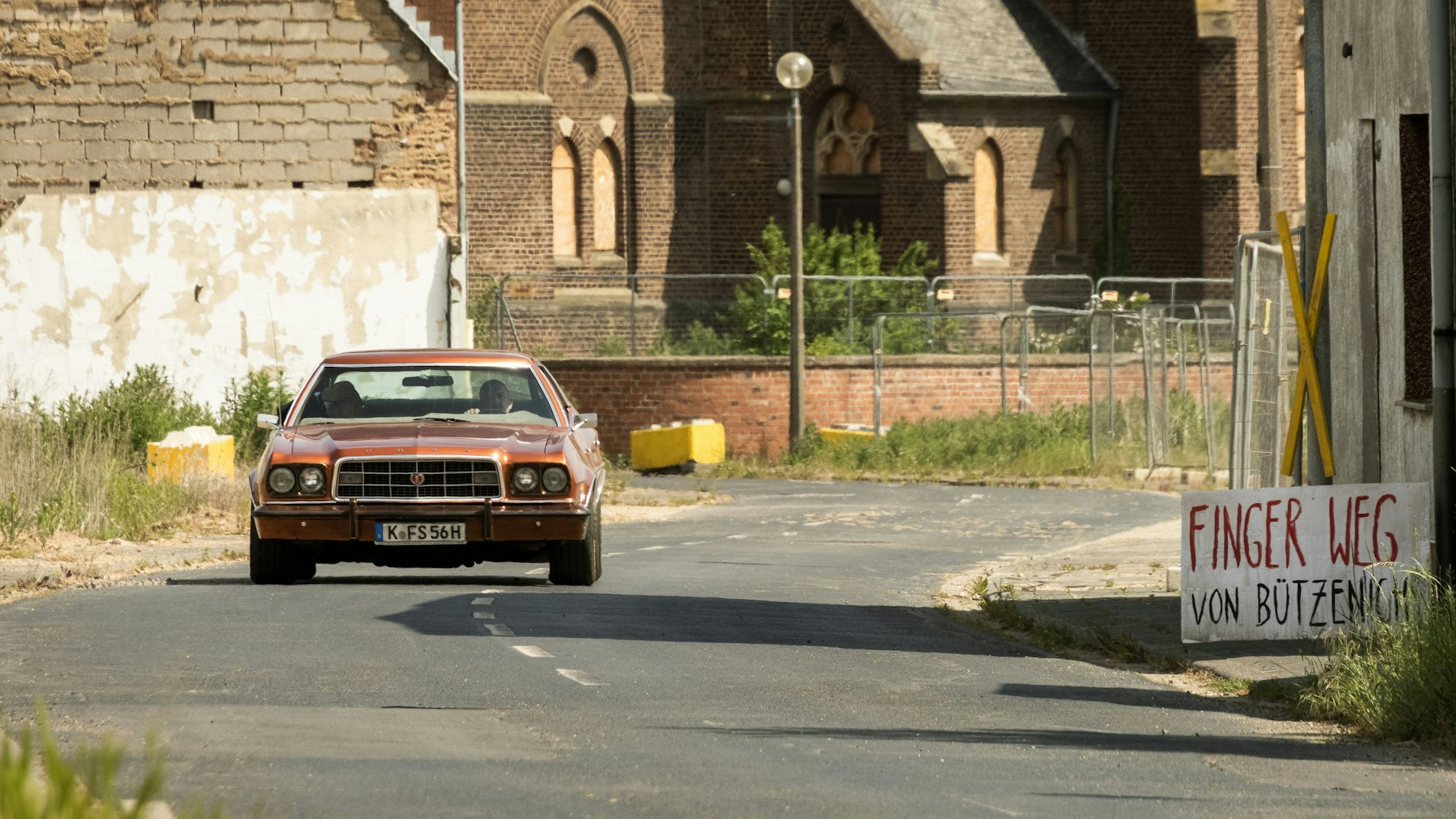 Ein roter Ford Gran Torino fährt mit Kölner Kennzeichen auf einer Straße entlang.