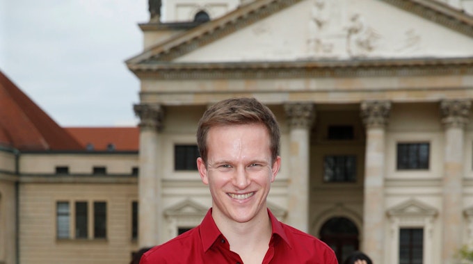 Der Marimbar-Spieler Christoph Sietzen steht am Gendarmenmarkt vor dem Berliner Konzerthaus. Er trägt ein leuchtend rotes Hemd und lacht.&nbsp;