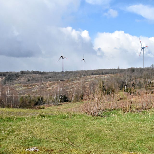 Vier Windkraftanlangen stehen auf einer Höhe. Es handelt sich um eine Fotomontage.