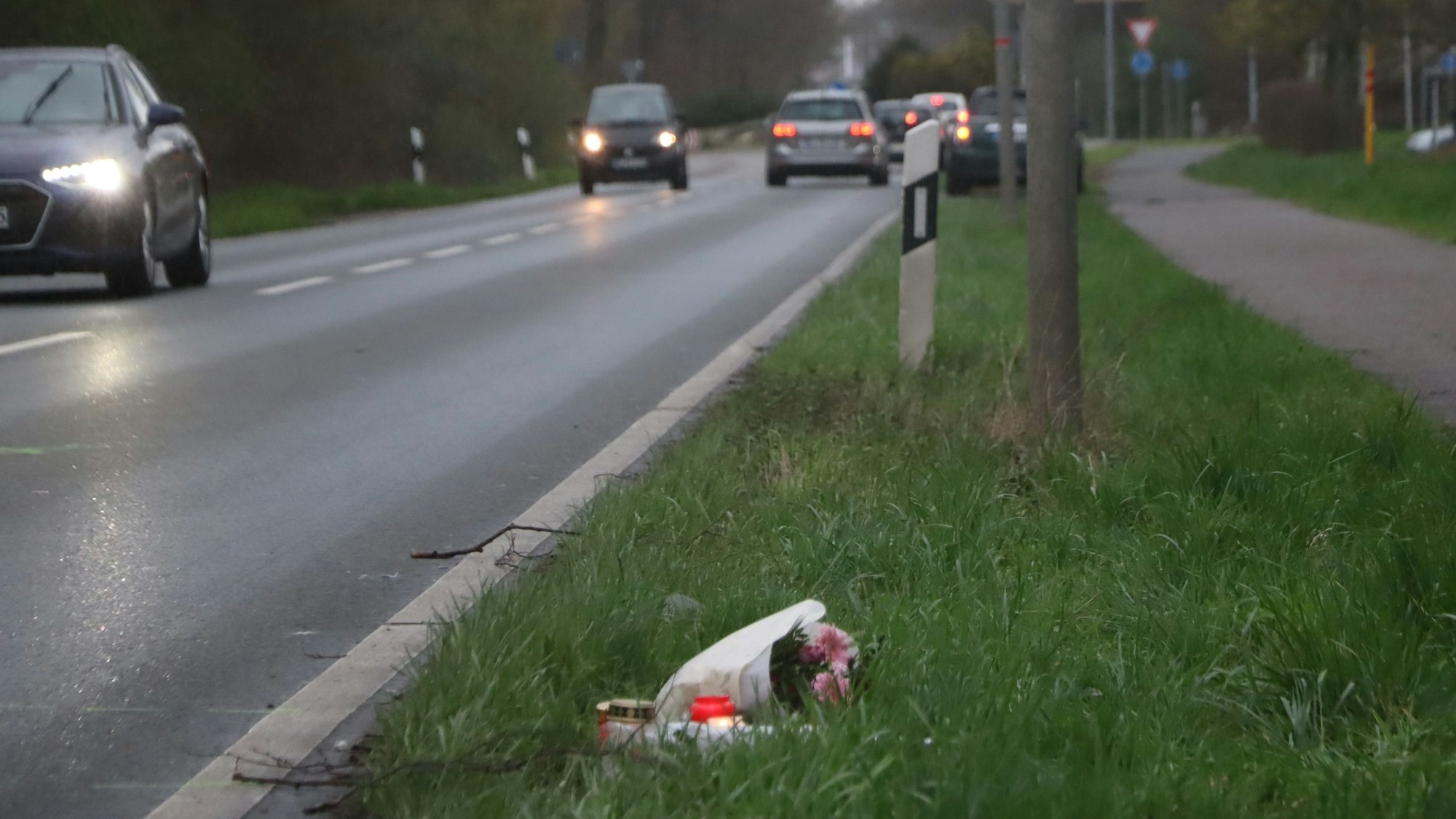Das Foto zeigt die Rodenkirchener Straße in Wesseling. Dort war in der Nacht auf Sonntag ein 20-Jähriger ums Leben gekommen. Im Grünstreifen liegen Blumen, Kerzen wurden aufgestellt.