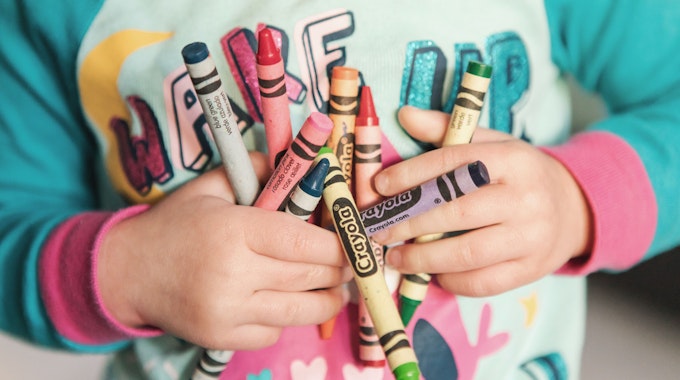 Ein Kind hält bunte Stifte in den Händen.