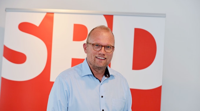 Jochen Ott steht vor einem SPD-Plakat und lächelt in die Kamera.