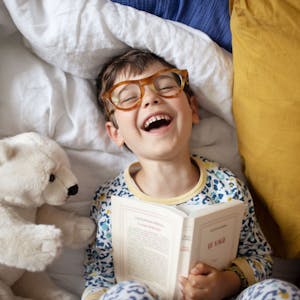 Portrait of a smiling little boy at home, he's wearing adult's glasses and pretending to read his parent's book