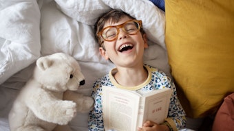 Portrait of a smiling little boy at home, he's wearing adult's glasses and pretending to read his parent's book